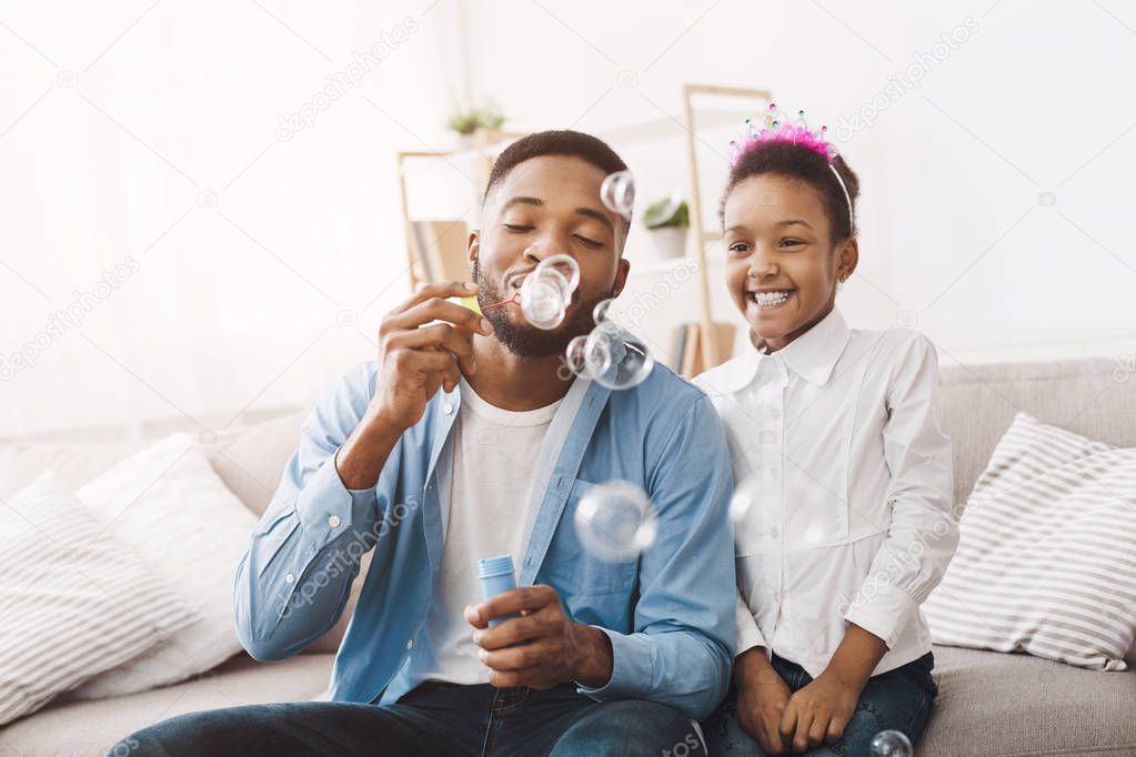 Father and daughter blowing soap bubbles at home