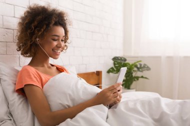 Mutlu kadın manifatura Smartphone, yatakta müzik dinleme