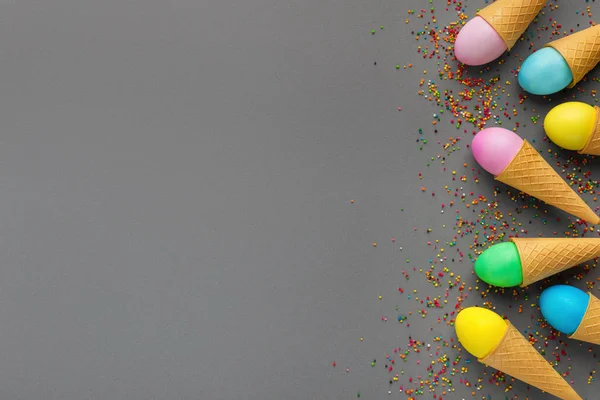 Ovos de páscoa coloridos em cones de waffle em fundo cinza — Fotografia de Stock