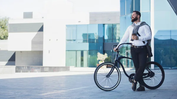 Jovem empresário segurando xícara de café enquanto se inclina em sua bicicleta — Fotografia de Stock