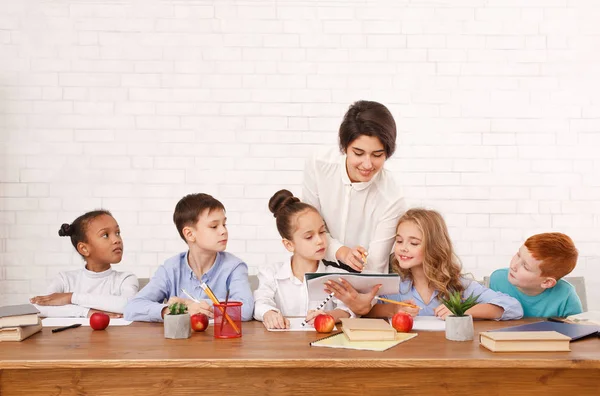 Leraar helpen kinderen schrijven van test in klas — Stockfoto