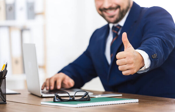 Successful businessman showing thumb up at workplace