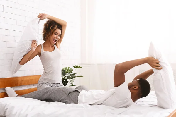 Cheerful loving couple is fighting by pillows in bed. — Stock Photo, Image
