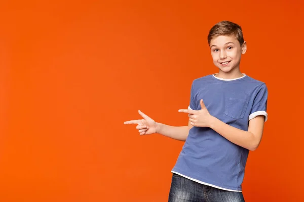 Niedlicher kleiner Junge, der auf orangefarbenem Hintergrund wegzeigt — Stockfoto