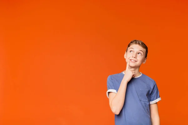 Kniffliger Junge denkt über einen Streich auf orangefarbenem Hintergrund nach — Stockfoto