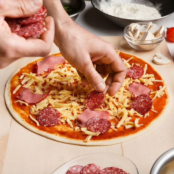 Koch legt Salami über Käse auf rohe Pizza — Stockfoto