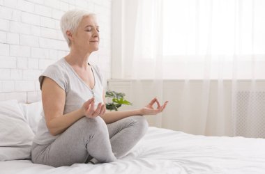 Üst düzey kadın yatakta evde yoga yaparken