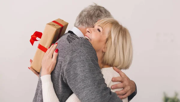 Hombre mayor dando regalo a la esposa, abrazando y sonriendo — Foto de Stock