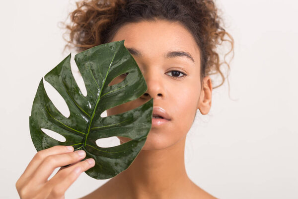 Woman with tropical leaf covering half of face