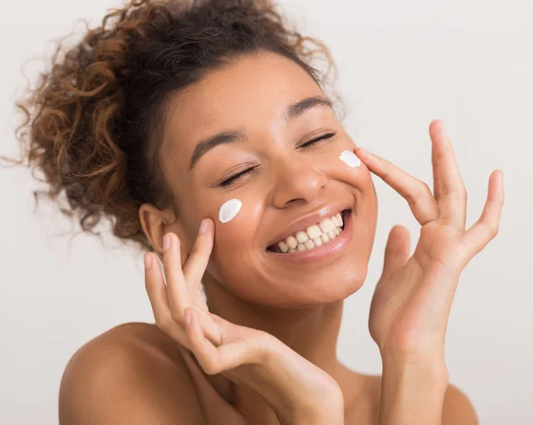 Felice donna afro-americana applicando crema viso, raccolto — Foto Stock