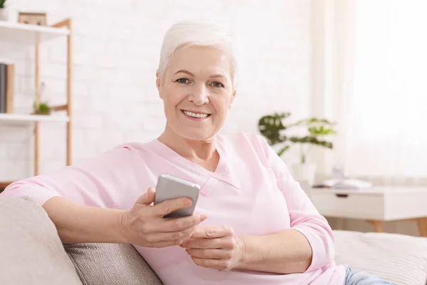 Веселая пожилая женщина использует свой смартфон дома — стоковое фото