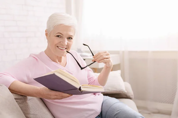 Vieille dame livre de lecture sur canapé à la maison — Photo