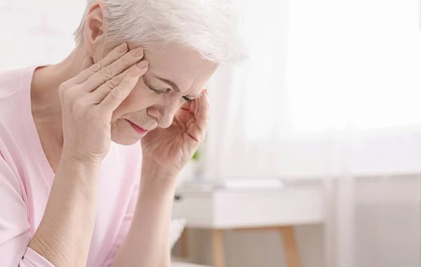 Senior woman having headache and touching her temples — Stock Photo, Image
