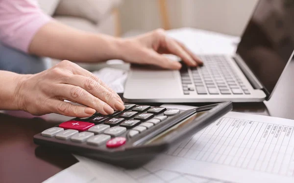 Femme âgée avec calculatrice comptant l'argent en dollars à la maison — Photo