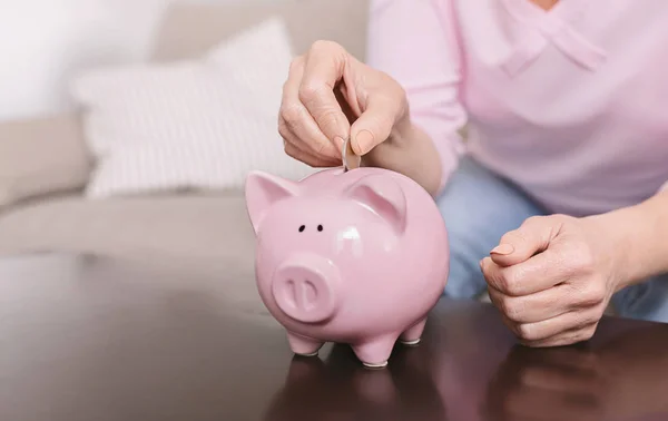 Velha mão feminina colocando moedas em rosa porquinho banco — Fotografia de Stock