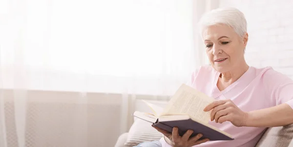 Old lady reading book on sofa at home — Stock Photo, Image