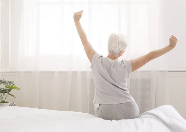Senior kobieta siedzi na jej łóżko rano — Zdjęcie stockowe