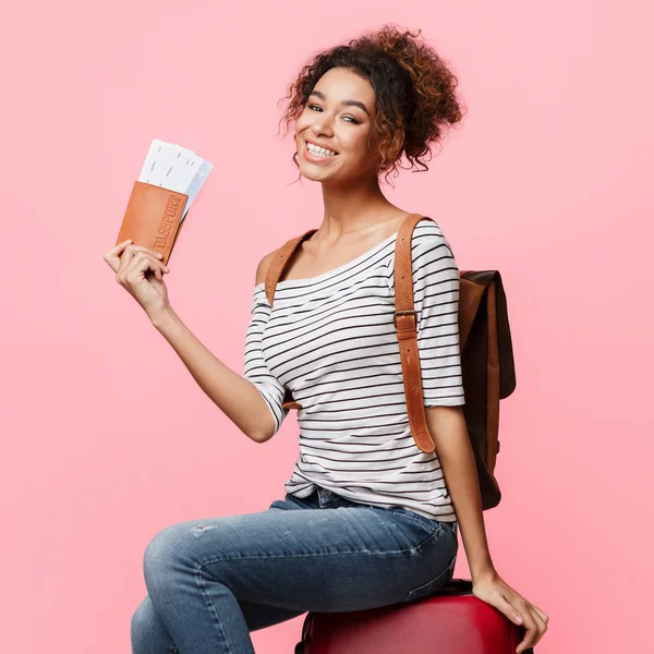 African-american woman holding passport with tickets, pink background