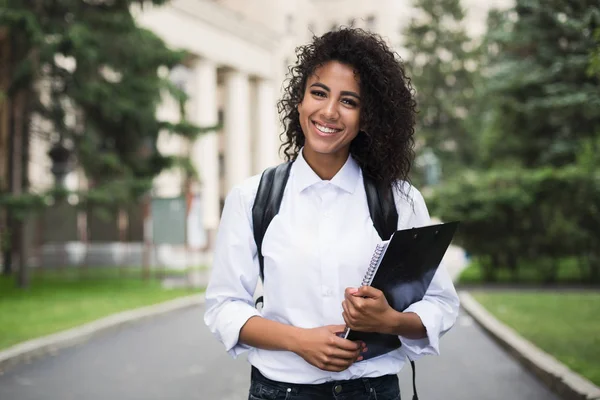 Menina estudante afro feliz segurando pastas e livros . — Fotografia de Stock