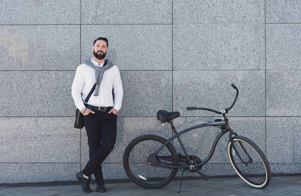 Businessman standing against building wall with his bicycle.