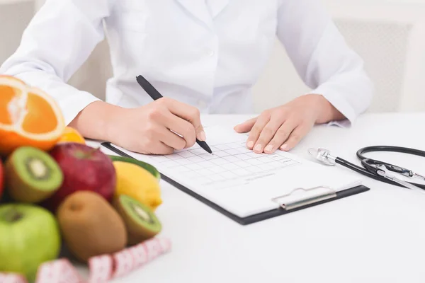 Nutricionista femenina médico escribir plan de dieta vegetal —  Fotos de Stock