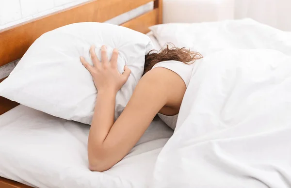 Mujer joven en la cama escondida bajo la almohada — Foto de Stock