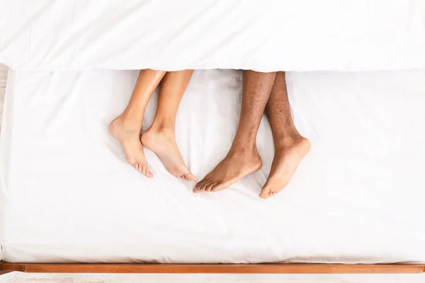 Любящие пары ног лежат на кровати под одеялом — стоковое фото
