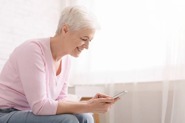 Veselý senior žena doma pomocí svého smartphonu — Stock fotografie