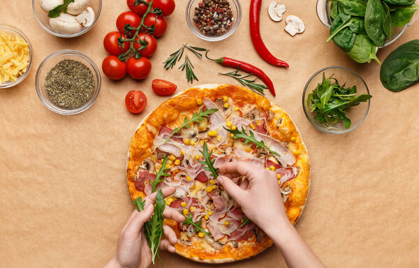 Woman adding rocket salad to pizza, top view