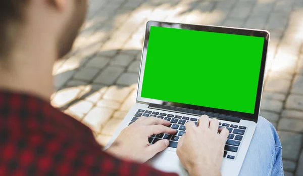 Millennial man typing on laptop with green screen