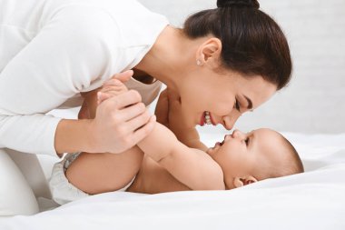 Genç kadın yatakta küçük bebeği ile oynarken