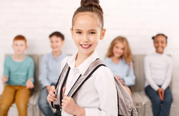 Escola menina carregando mochila com amigos no fundo — Fotografia de Stock