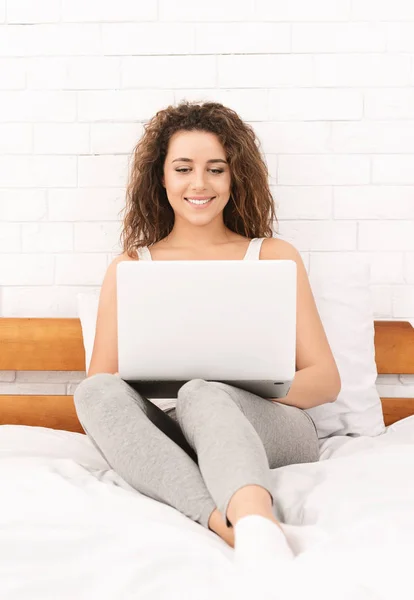Mujer sentada en la cama y trabajando en el portátil —  Fotos de Stock