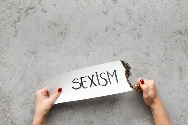 Женщина сжигает бумажную открытку словом "сексизм" — стоковое фото