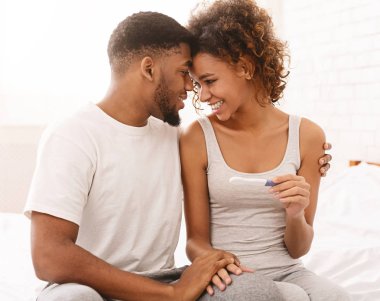 Happy couple holding positive pregnancy test on bed clipart