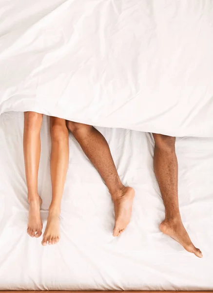 Masculino y femenino piernas bajo edredón acostado en la cama —  Fotos de Stock