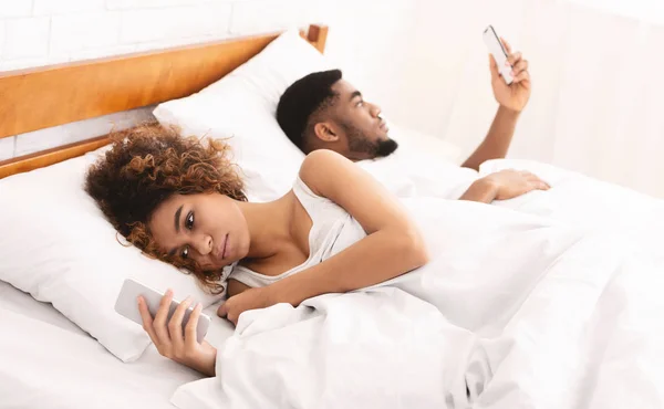 Millennial couple lying on bed back to back with smartphones — Stock Photo, Image