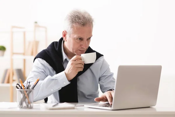 Ώριμος άνδρας εργάζονται για το laptop και πίνοντας τσάι — Φωτογραφία Αρχείου