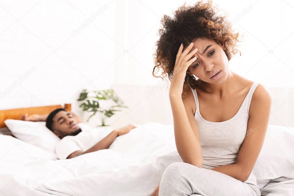 Unhappy black woman suffering from headache, sitting in bed