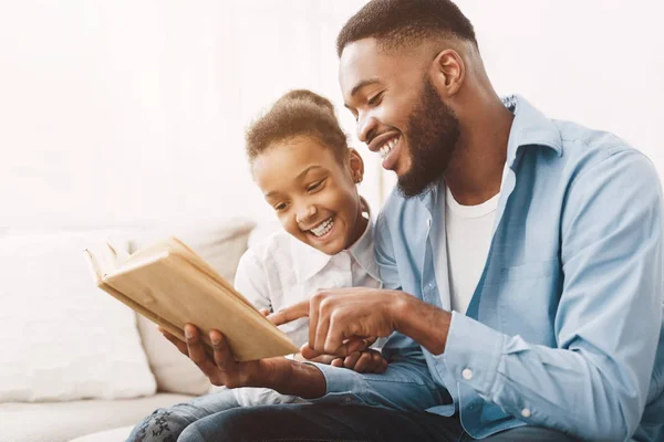 Padre e hija afroamericanos disfrutando leyendo un libro juntos — Foto de Stock