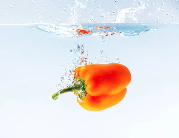 Paprika arancione colorata in spruzzi d'acqua su sfondo blu — Foto Stock