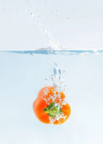 Páprica laranja colorida em salpicos de água no fundo azul — Fotografia de Stock