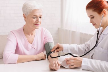 Doctor checking blood pressure of senior patient clipart