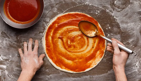 Человек добавляет томатный соус к итальянской базе пиццы — стоковое фото