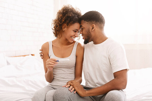 Happy couple holding positive pregnancy test on bed