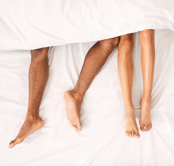 Male and female legs under duvet lying on bed