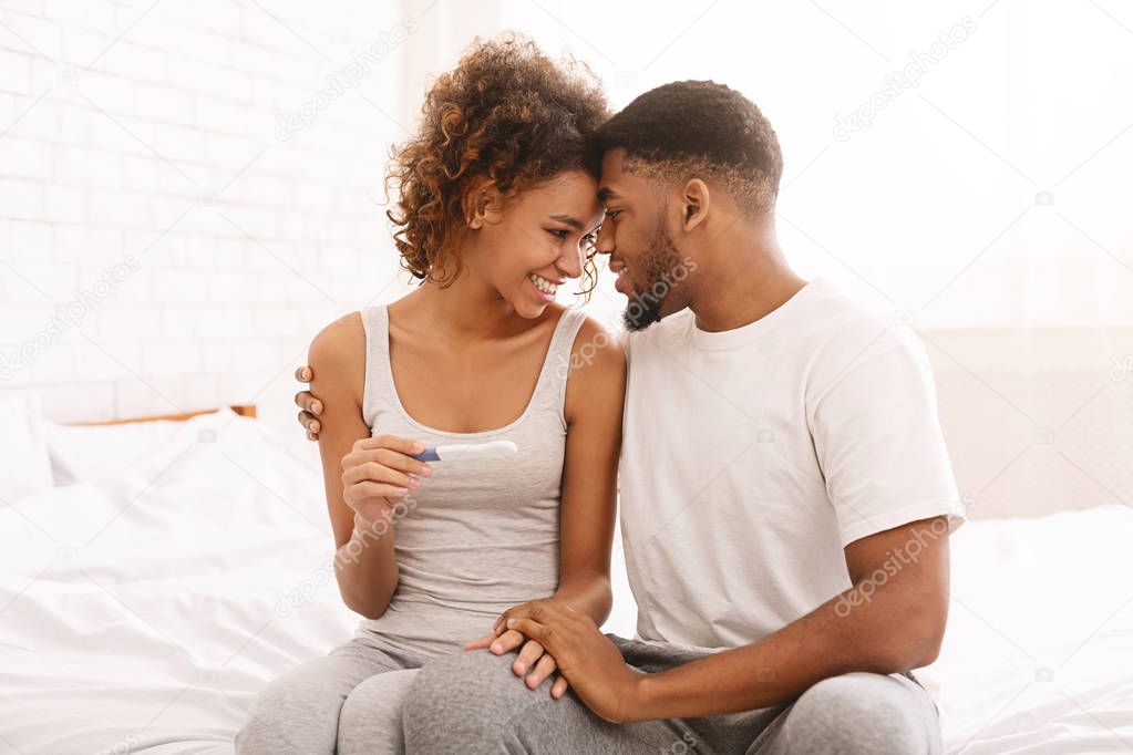 Happy couple holding positive pregnancy test on bed