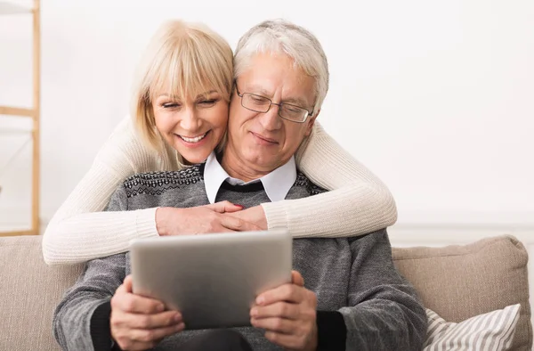 Bejaarde echtpaar met behulp van digitale tablet in woonkamer — Stockfoto