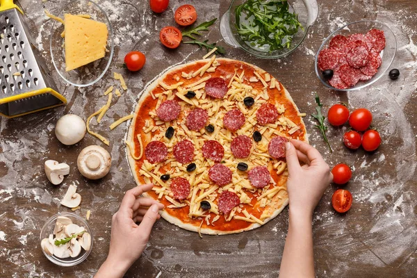 Frau bereitet Pizza zu und dekoriert sie mit Salami — Stockfoto