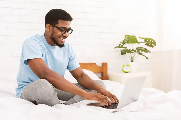 Programmatore afro-americano che digita sul computer portatile a letto — Foto Stock